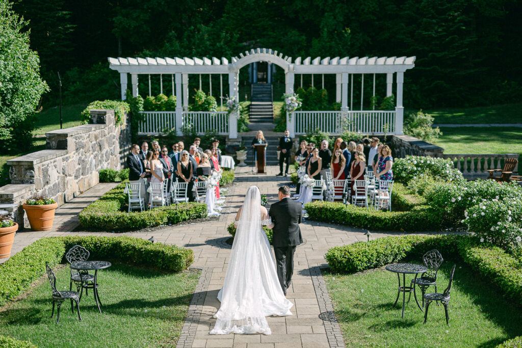 La mariée marche avec son père dans l'allée des jardins lors de la cérémonie de mariage.