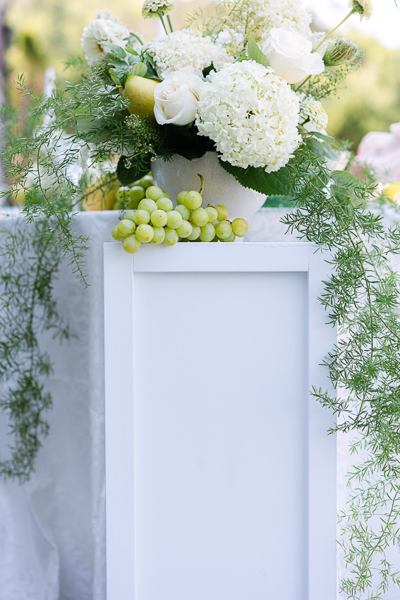 Un vase contenant des leurs déposé sur une colonne blanche, avec des raisins. Un décor chaleureux et joyeux pour un mariage, signé Myriades & Co.